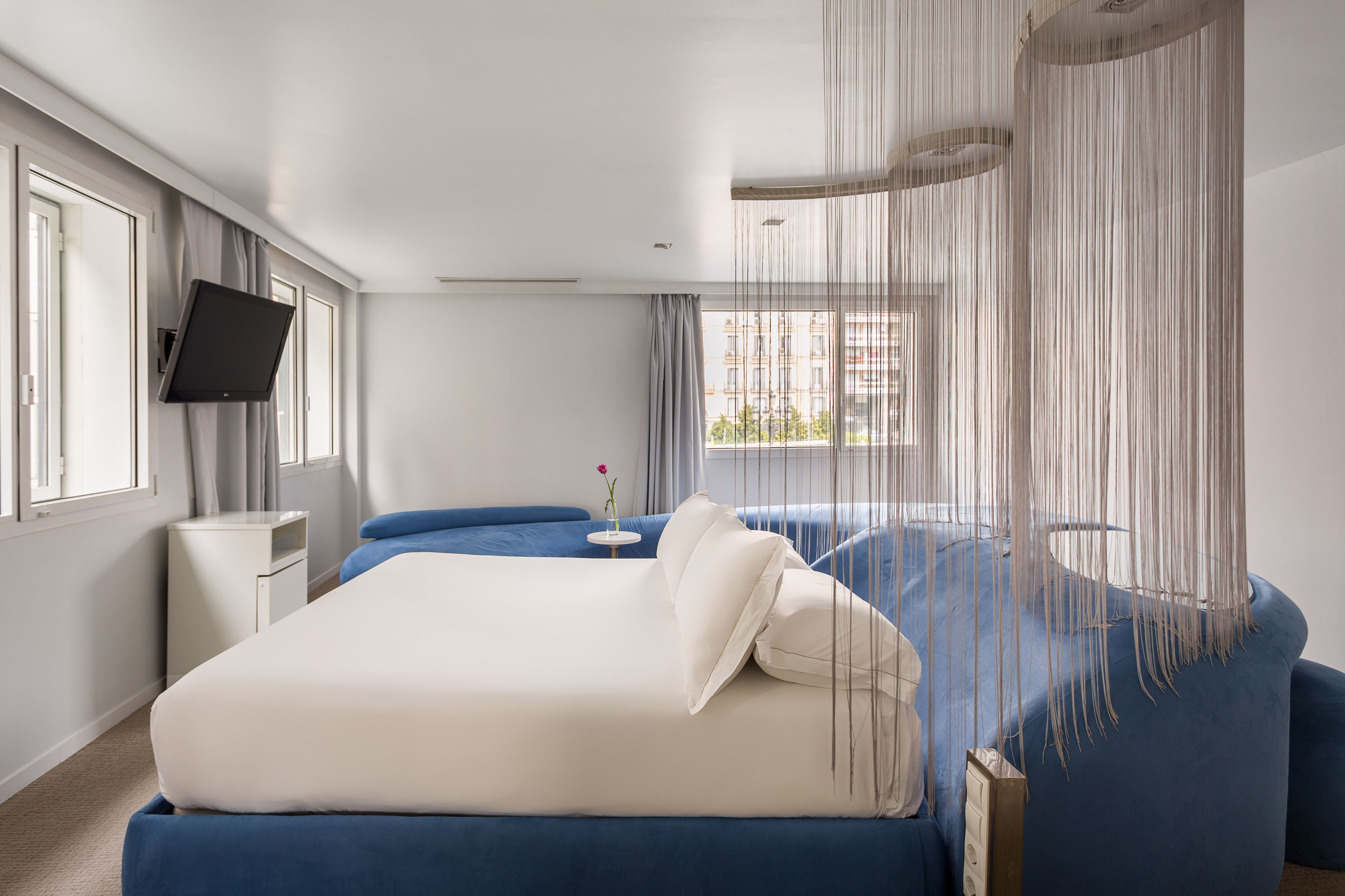 Habitación de hotel moderna con una cama grande, una mesita de noche, un televisor y vistas a edificios.