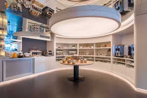 Enjoy a meal at this modern space with a central table surrounded by kitchen appliances and food displays.