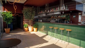 Una zona de bar con pared de azulejos verdes, plantas en macetas y taburetes.