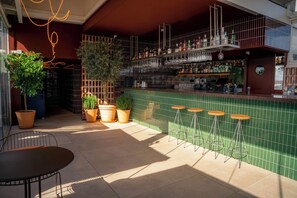 Angolo bar con parete rivestita di piastrelle verdi, piante in vaso e sgabelli.