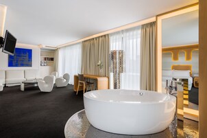Una camera d'albergo moderna con una grande vasca da bagno, un divano, un tavolino da caffè e una TV fissata al muro.