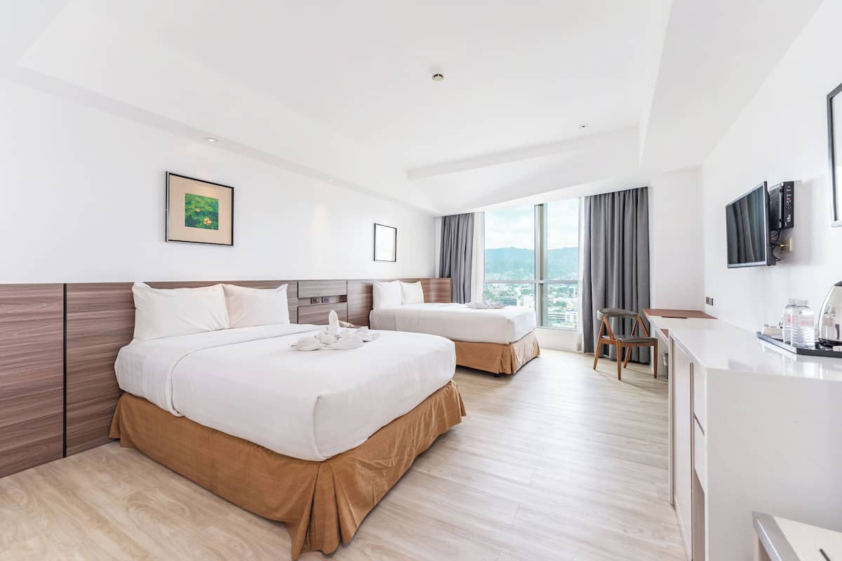 A hotel room with two beds, a desk, a chair, a TV, and a window with a city view.