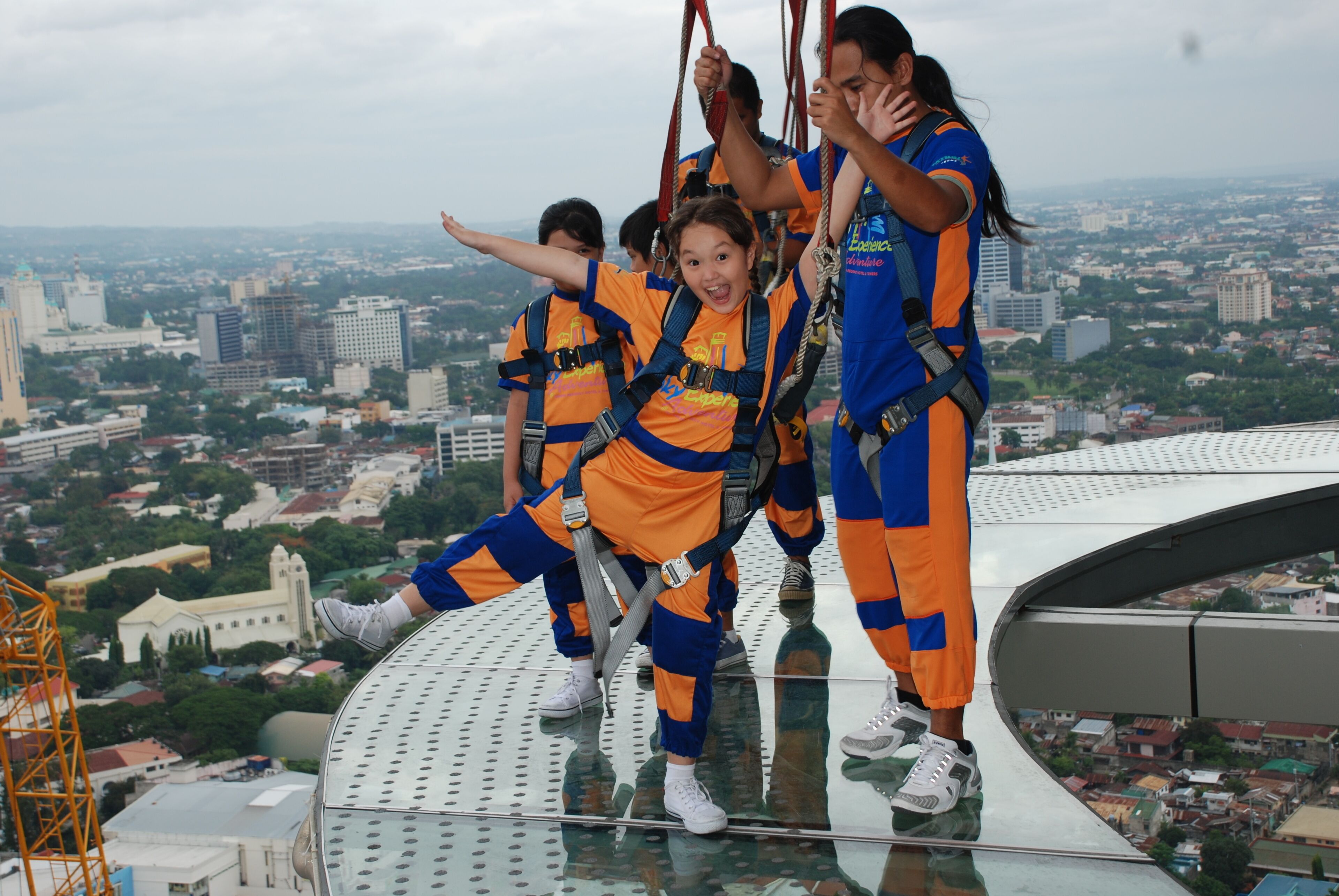 A group of people on a glass bridge with a cityscape in the background.