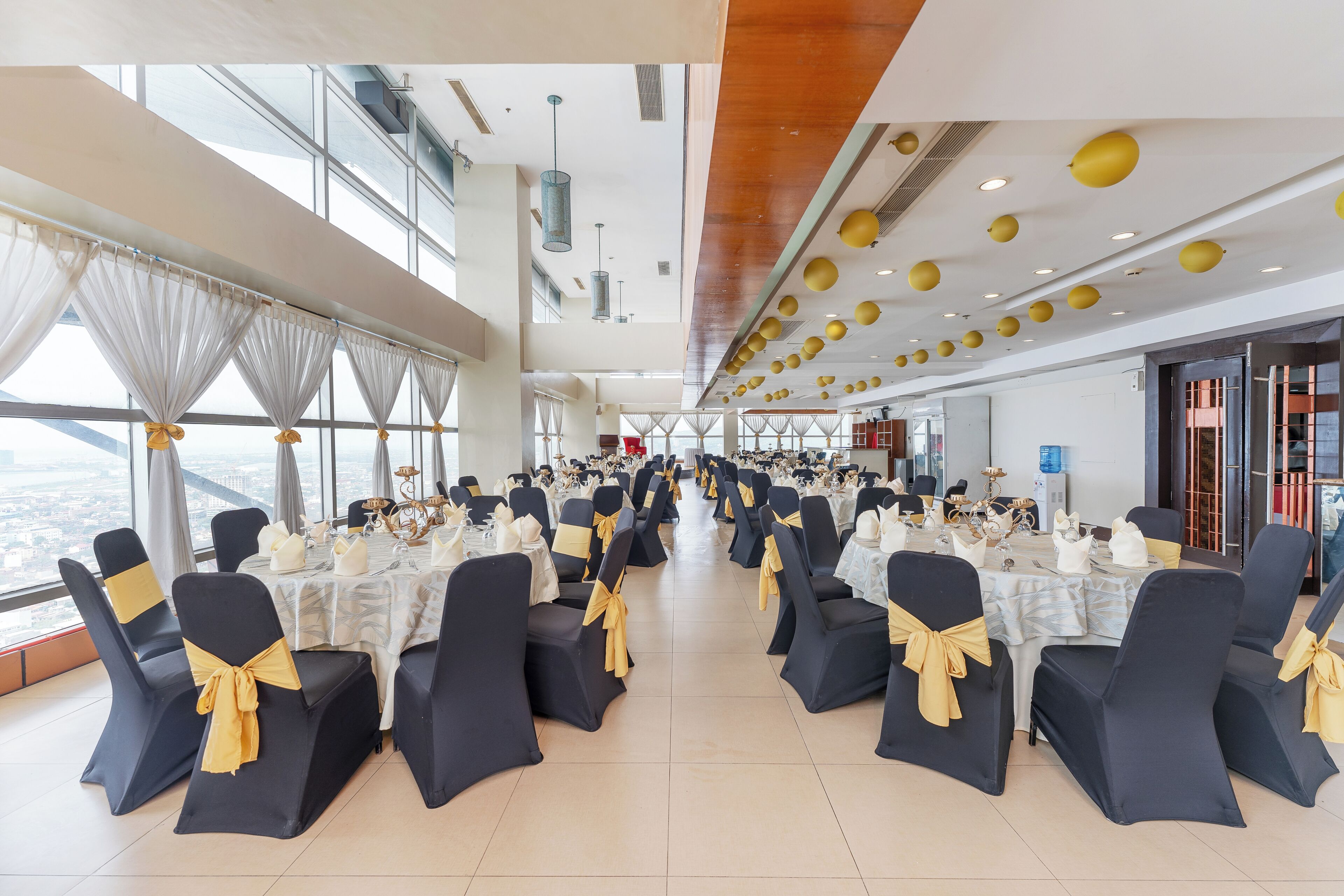 A spacious banquet hall with high ceilings, large windows, and tables set for a formal event.