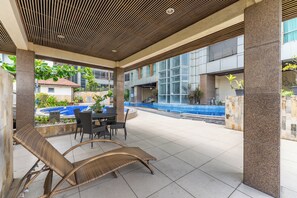 A covered outdoor area with a pool, lounge chairs, and a dining table.