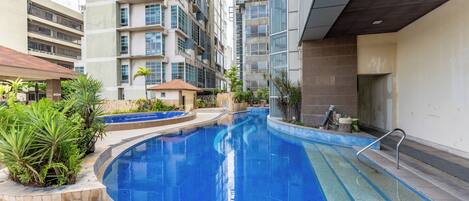 Una piscina rodeada de un área ajardinada con plantas y un edificio de varios pisos al fondo.