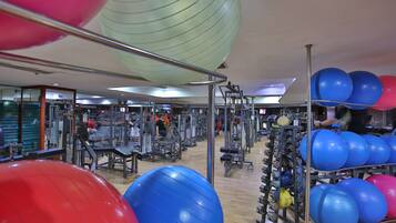Ein Fitnessstudio mit Trainingsgeräten, einem Ballgestell und einer Person beim Training.