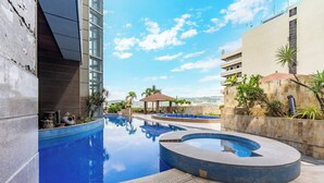 A swimming pool with a curved design, surrounded by buildings and palm trees. - Crown Regency Hotel and Towers (Cebu City)