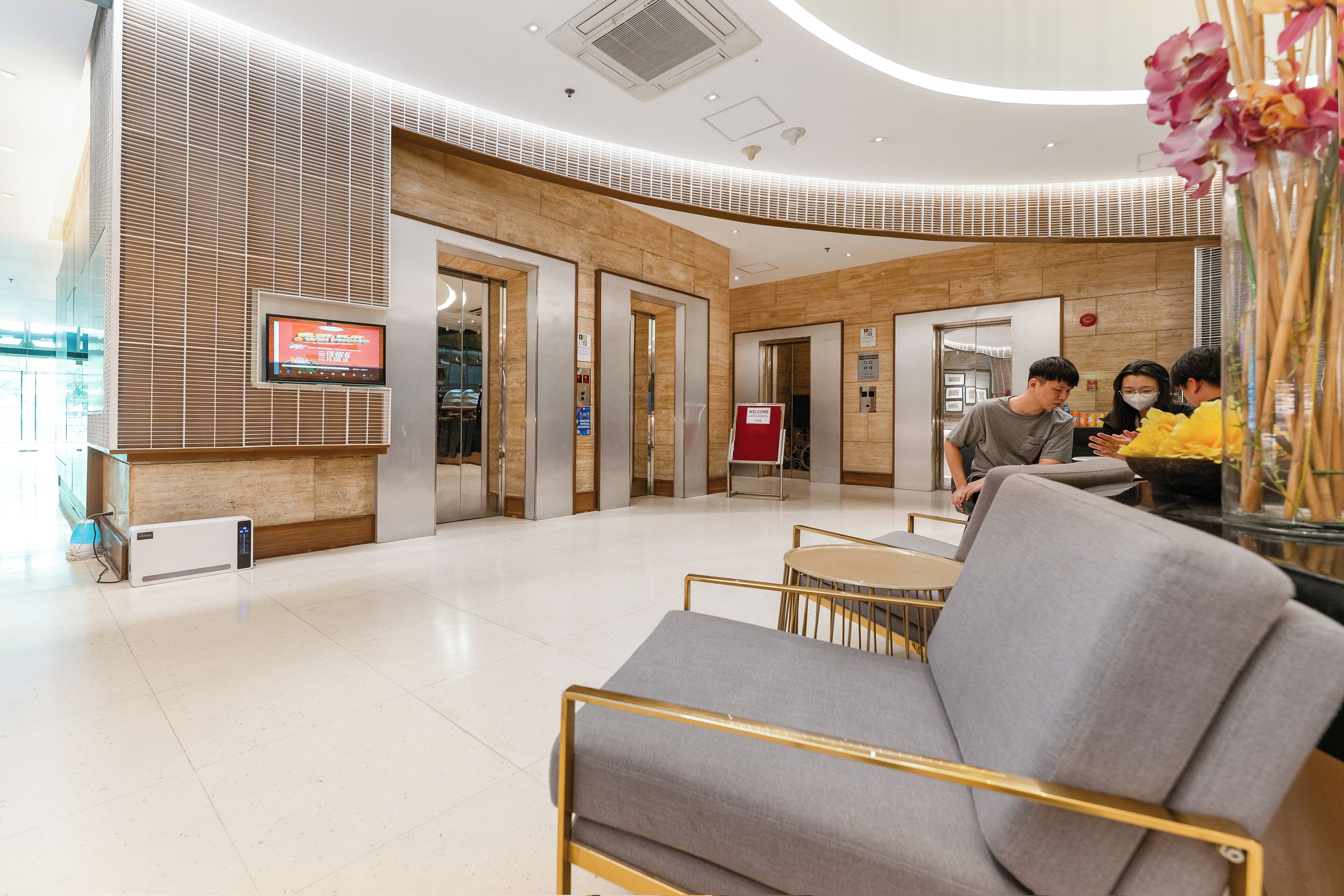 A modern hotel lobby with a reception desk, seating area, and elevators.