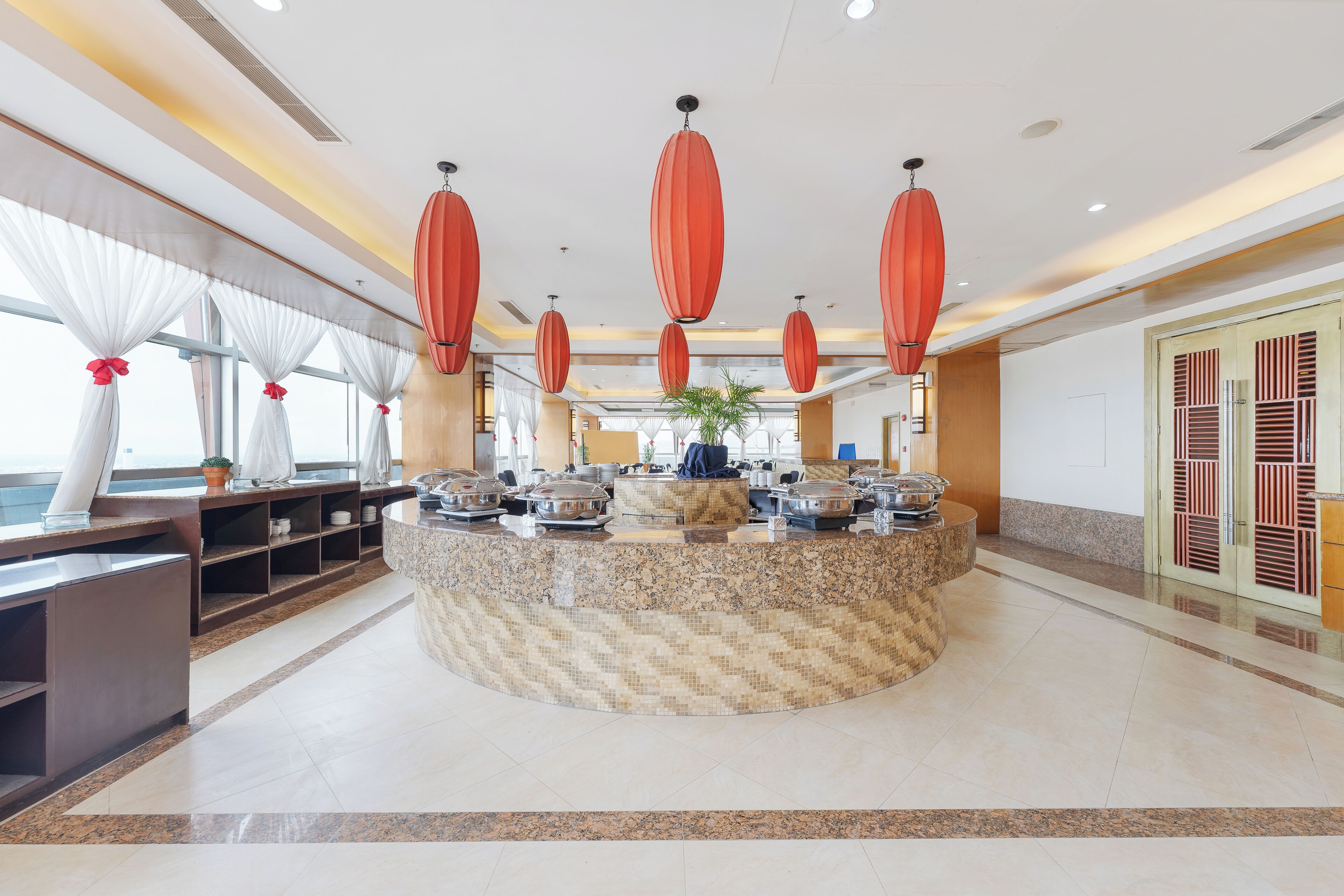 Eine Hotellobby mit einer zentralen Rezeption, einer großen Pflanze im Topf und einer traditionellen chinesischen Tür rechts.