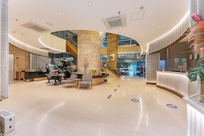 A spacious lobby with a reception desk, seating area, and a staircase leading to upper floors.