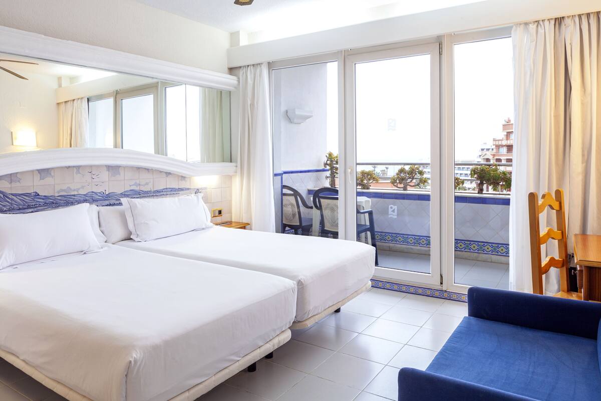 Une chambre d’hôtel avec deux lits, un balcon donnant sur la ville et un canapé bleu.