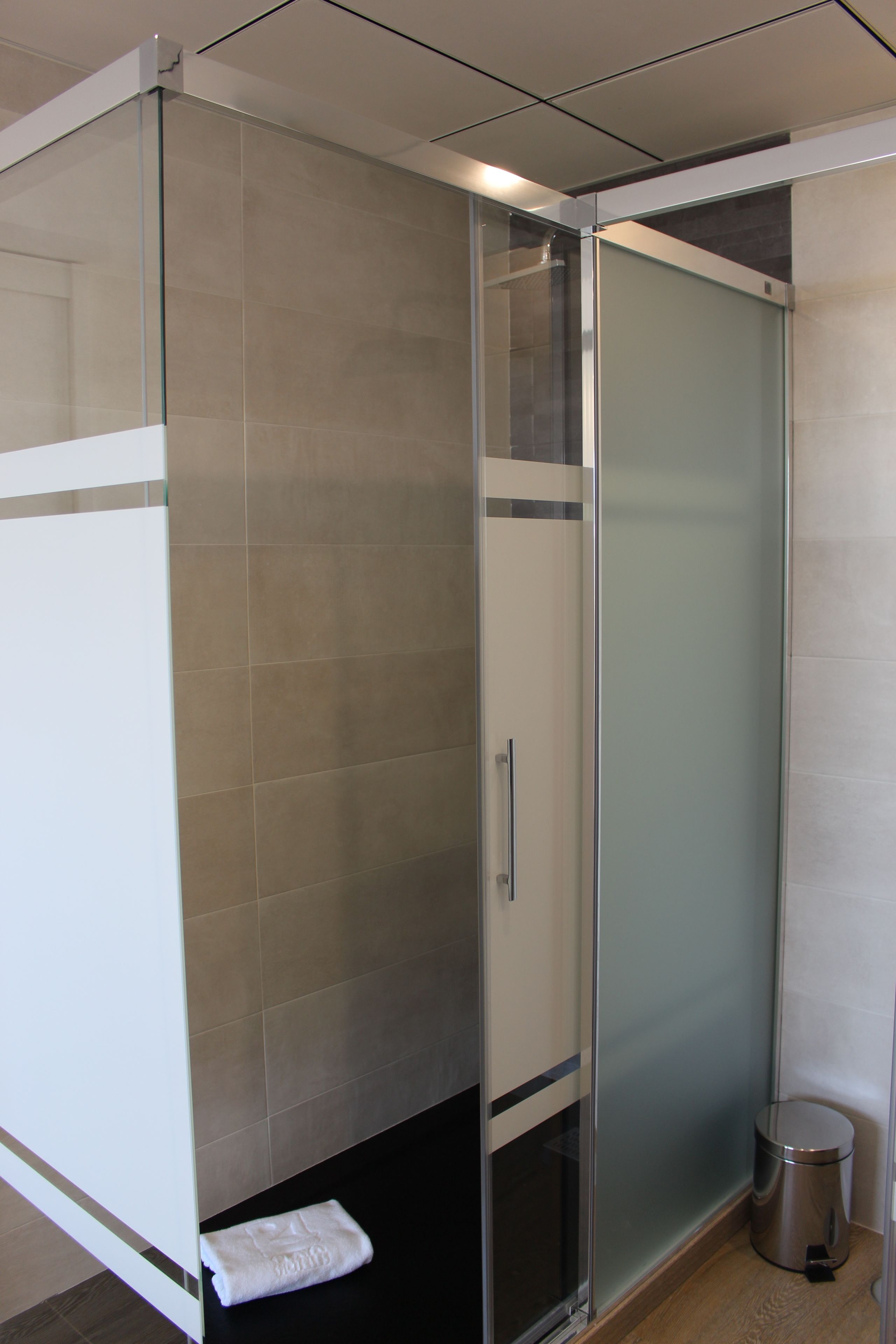 Un baño moderno con cabina de ducha de vidrio, una toalla blanca en el suelo y un cubo de basura.