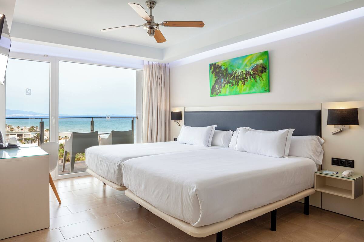 Une chambre d’hôtel avec un grand lit, un bureau et une chaise. Elle dispose d’un balcon avec vue sur l’océan.