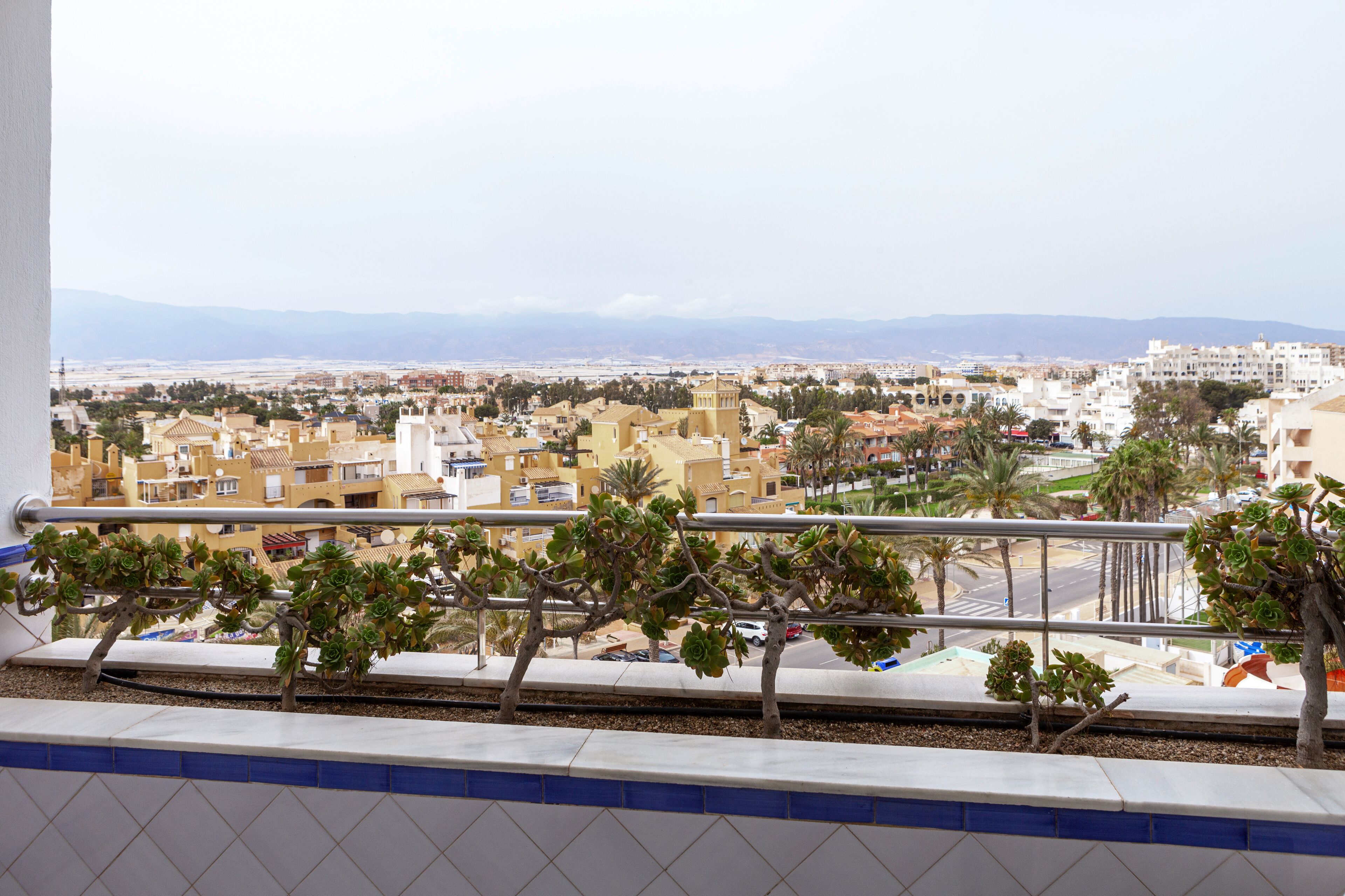 A balcony with a view of a cityscape, including buildings and mountains in the distance.