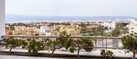 A balcony with a view of a cityscape, including buildings and mountains in the distance.