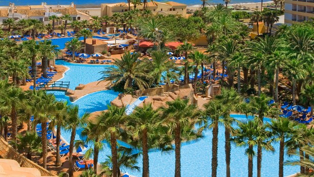 A resort with a central swimming pool surrounded by palm trees and sun loungers, with a view of the ocean. - Playasol Hotel (Roquetas de Mar)
