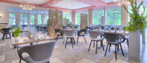 Ein modernes Restaurant mit mehreren Tischen, Stühlen und großen Fenstern, die einen Blick auf Grünflächen bieten.
