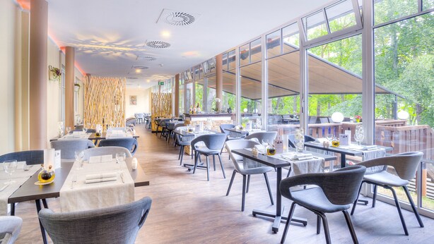 A modern restaurant with high ceilings, large windows, and a long dining area with tables and chairs. - Ostseehotel Villen Im Park – ein Rovell Hotel (Heringsdorf)