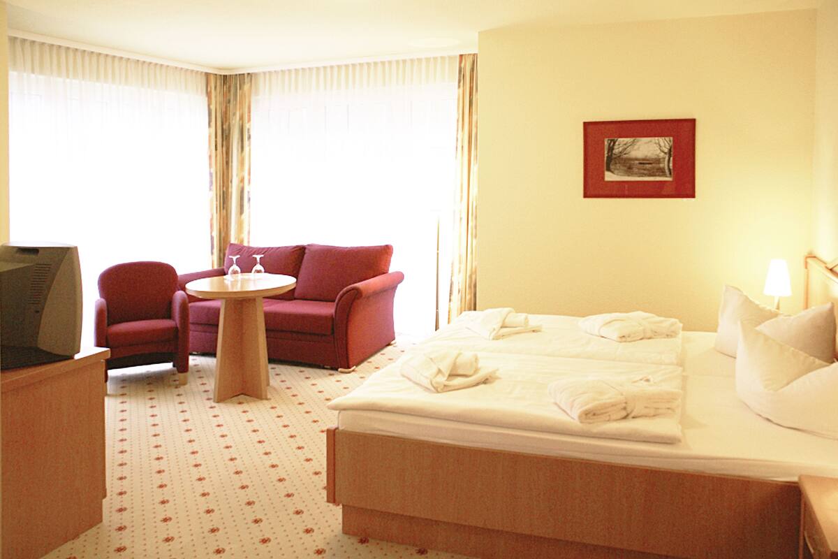 Una habitación de hotel con una cama, un sillón rojo, una mesita redonda y un televisor.