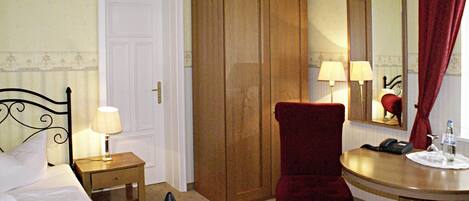 Une chambre d’hôtel comprenant un lit, une armoire en bois, un bureau avec une chaise, une table de chevet avec une lampe et un miroir au mur.