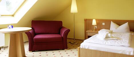 Ein Hotelzimmer mit einem Bett, einem roten Sessel, einem runden Tisch und einer Stehlampe.