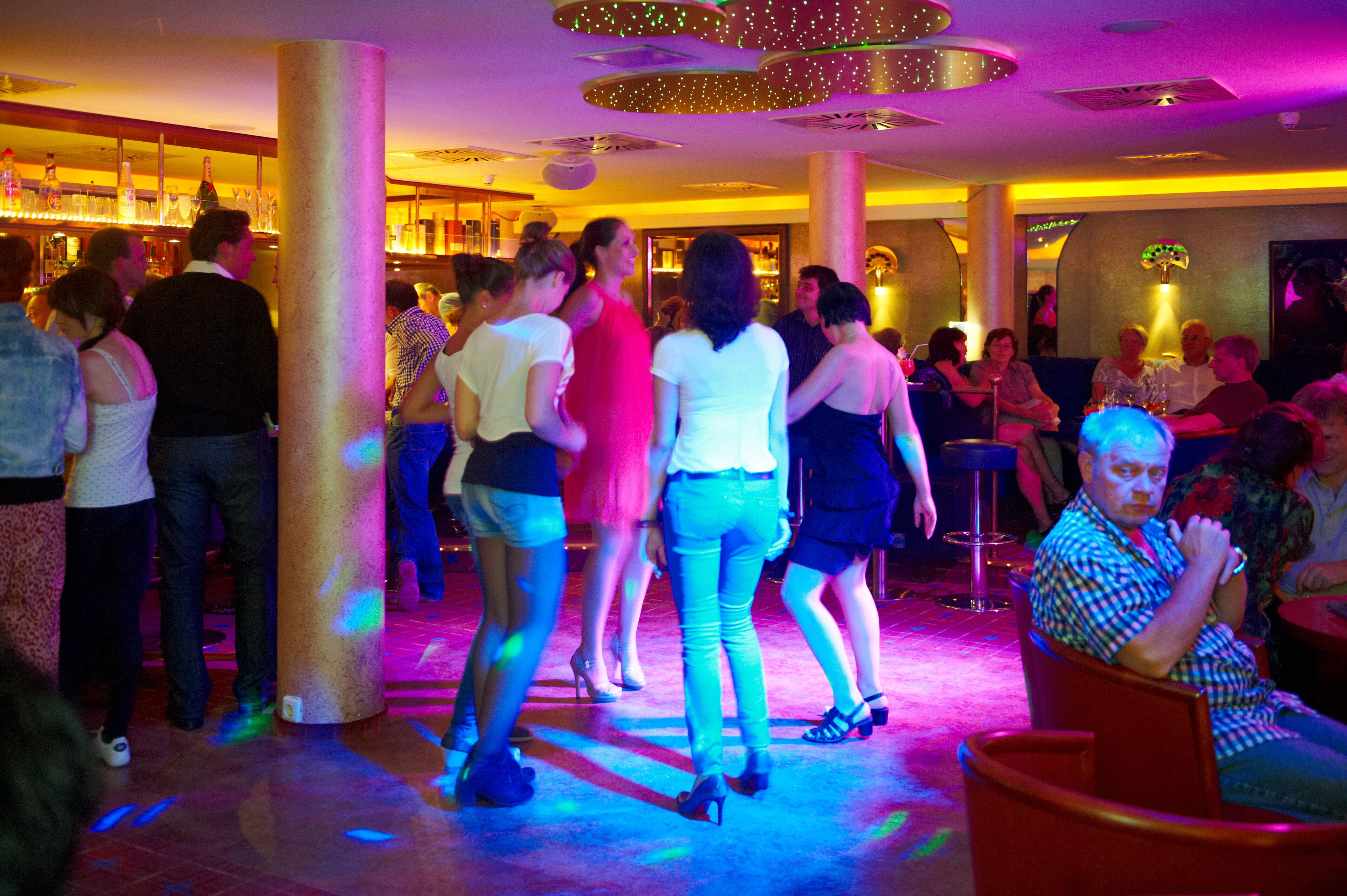 A crowded indoor space with people standing and sitting, possibly a bar or social area.
