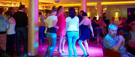 Un espacio interior concurrido, con gente de pie y sentada, posiblemente un bar o zona social.