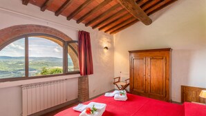 A room with a red bedspread, a wooden wardrobe, a window with a view of the countryside, and a radiator. - Fattoria Querceto (Barberino Tavarnelle)
