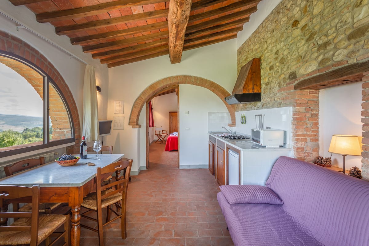 A kitchen with a stone wall, wooden beams, and a dining area with a table and chairs.