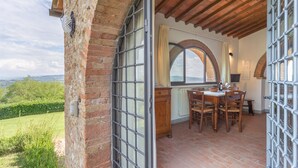 A rustic kitchen with a view of the countryside, a dining area with wooden furniture, and a brick exterior wall. - Fattoria Querceto (Barberino Tavarnelle)