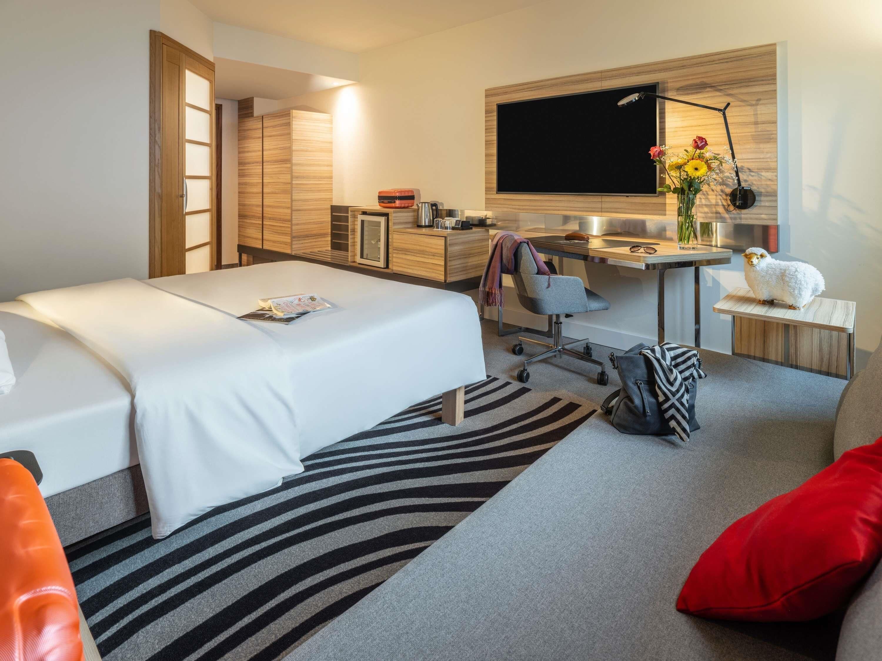 Ein Hotelzimmer mit Bett, Schreibtisch, Stuhl, Sofa und Fernseher.