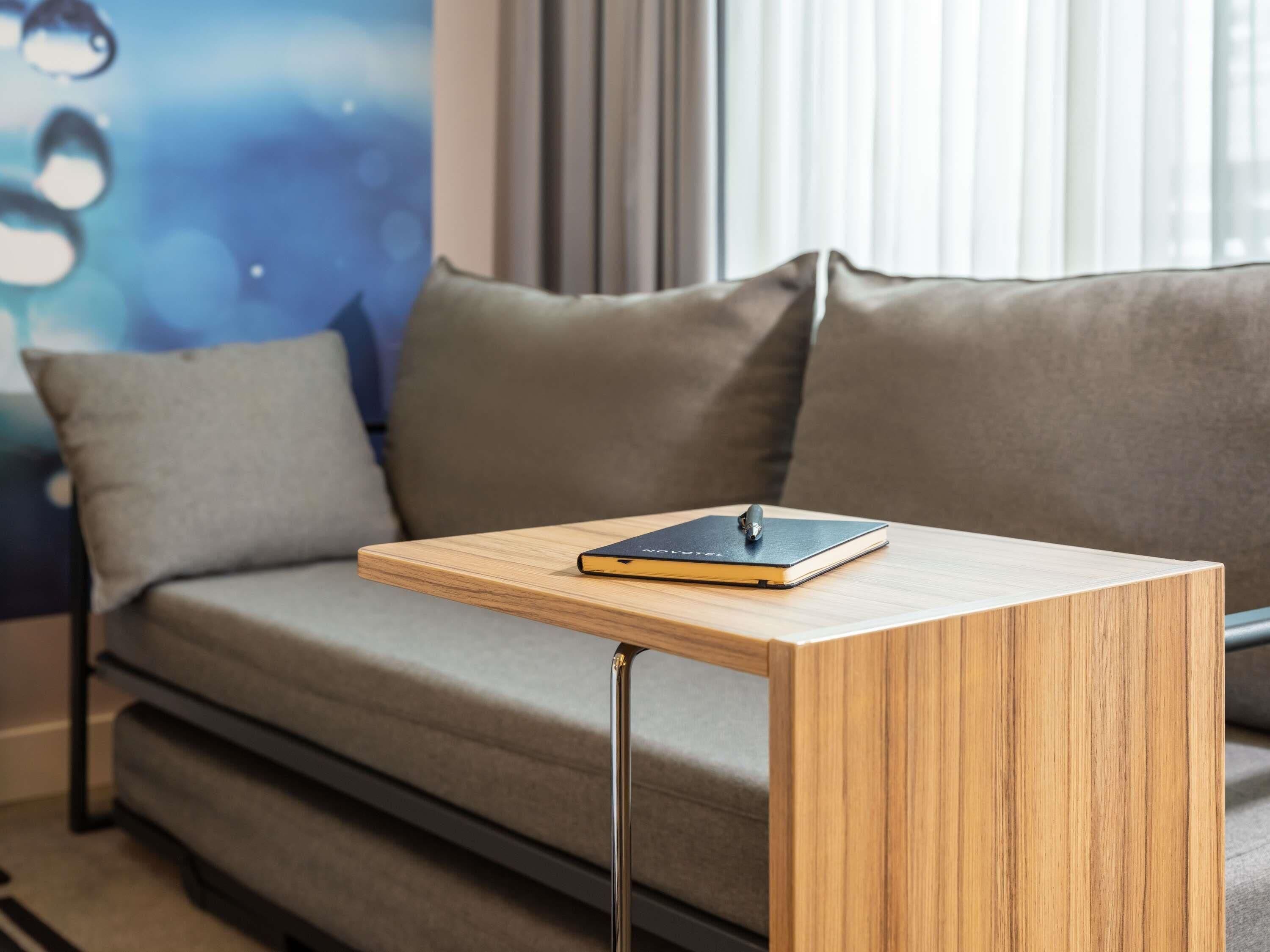 A modern living room with a grey sofa, a wooden side table, and a notebook.
