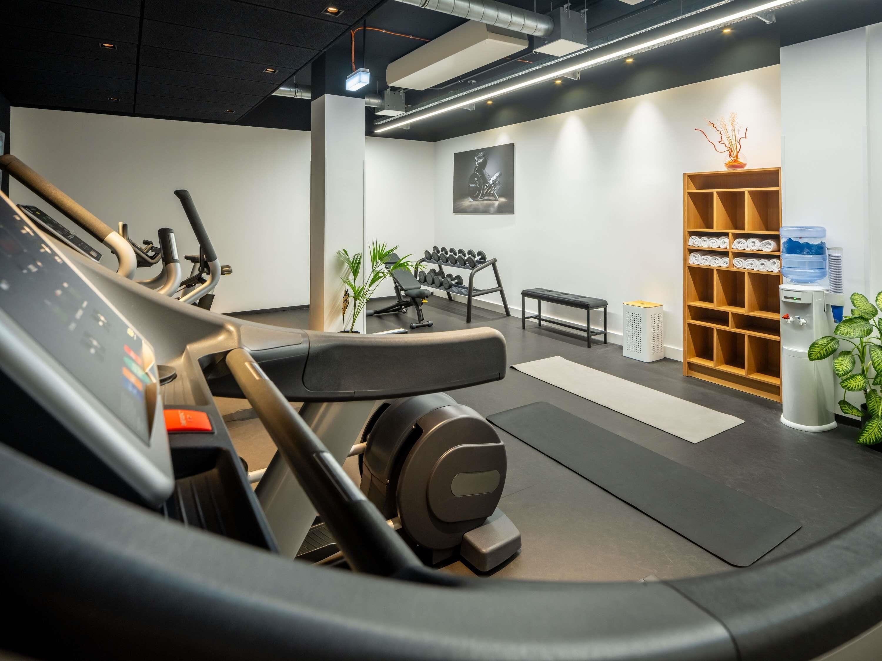 A gym with exercise equipment, a water dispenser, and a wall-mounted shelf with towels.
