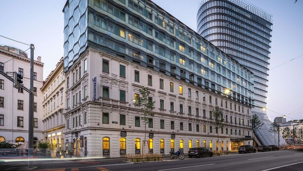 Un hotel moderno con fachada clásica, ventanas amplias y una llamativa torre de vidrio curva.