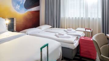 A hotel room with two beds, a desk, a chair, and a red suitcase.