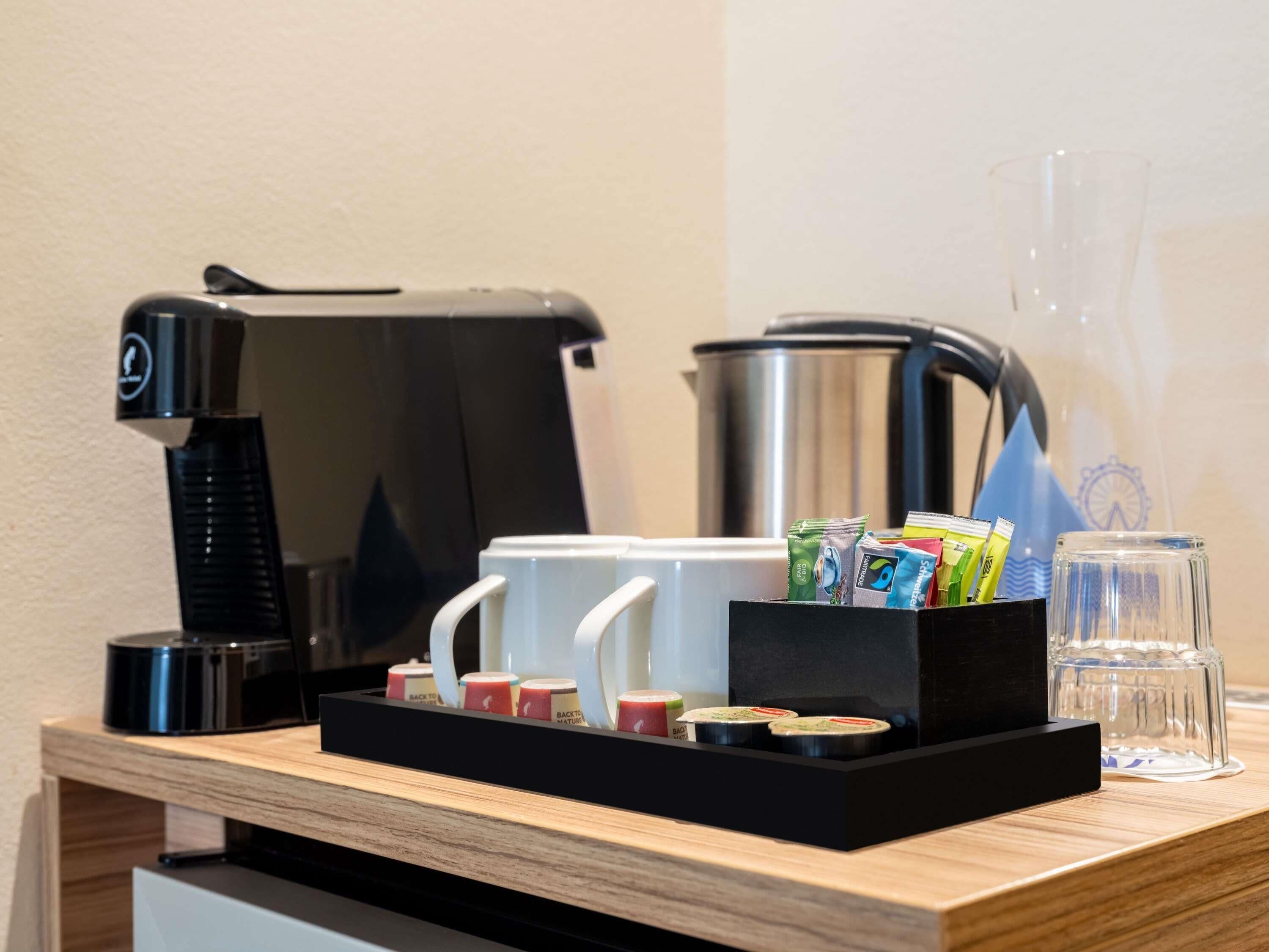 A coffee station with a coffee maker, a thermos, a glass, and a tray with coffee pods.