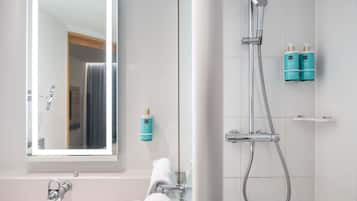 A bathroom with a mirror, a shower, and two toiletry bottles on the wall.