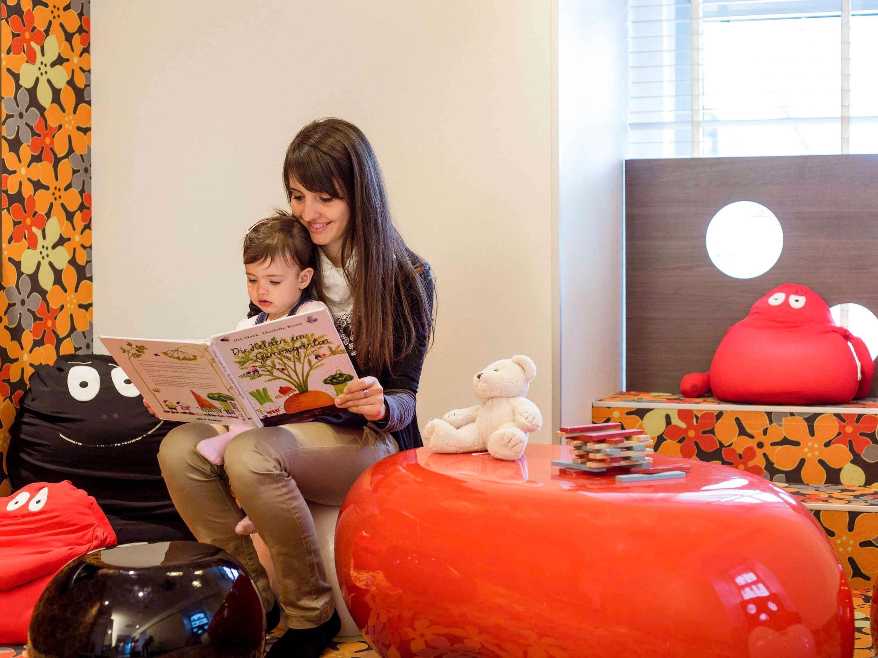 A room with a child reading a book, a white teddy bear, and colorful bean bag chairs.