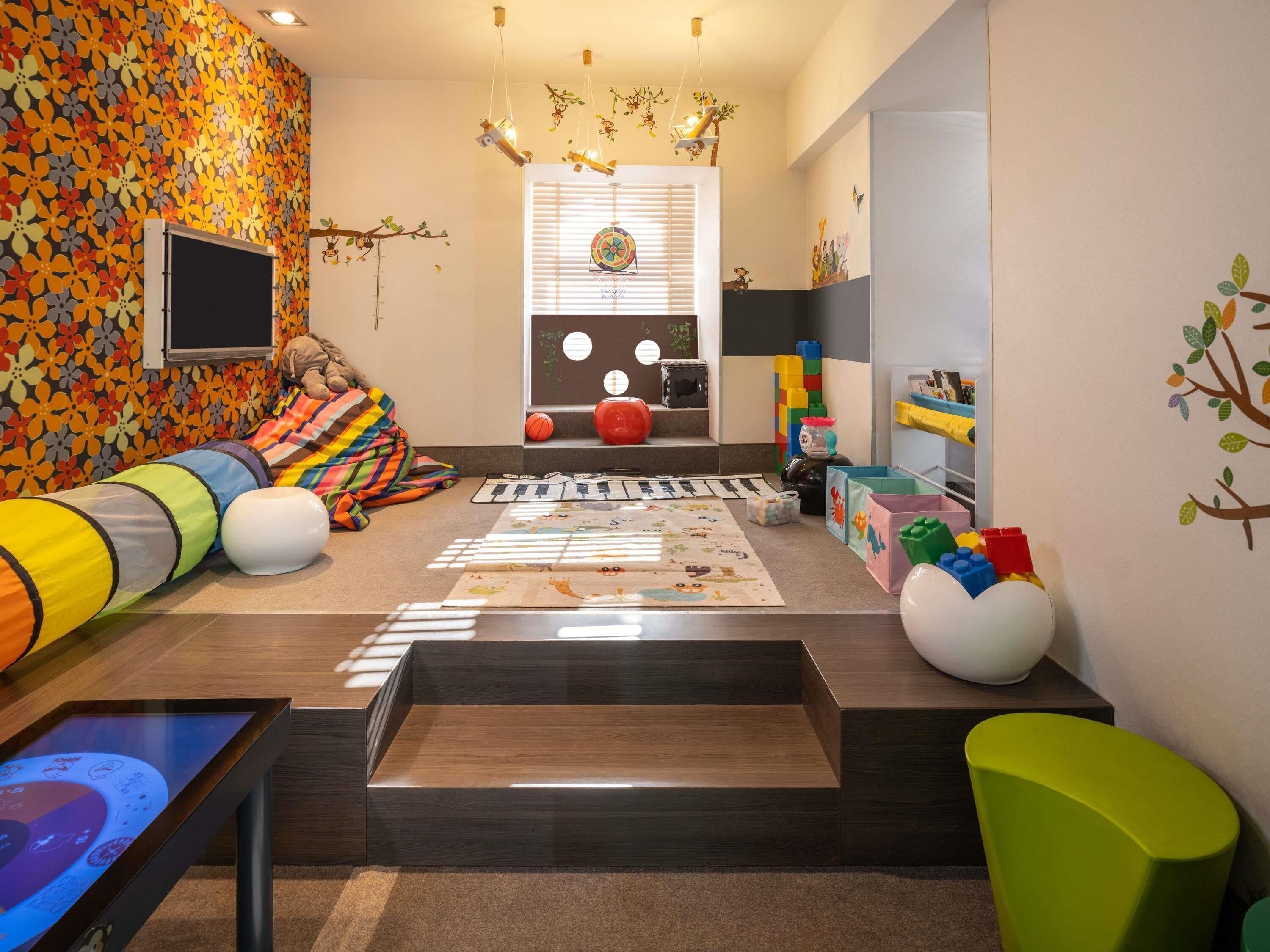 A playroom with a colorful wall, a play mat, toys, and a window with blinds.