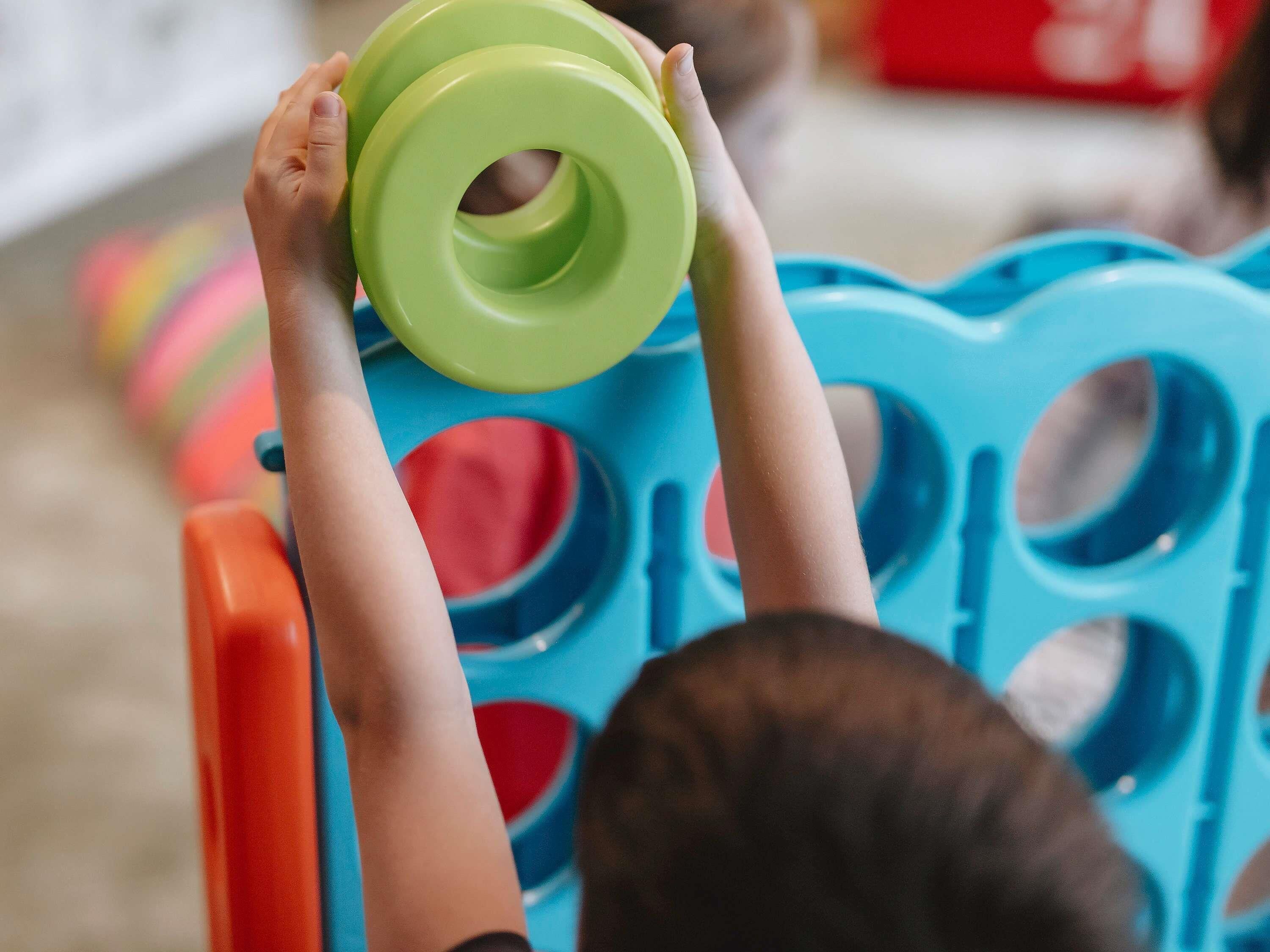 A child holding a green object above a blue chair with circular cutouts.