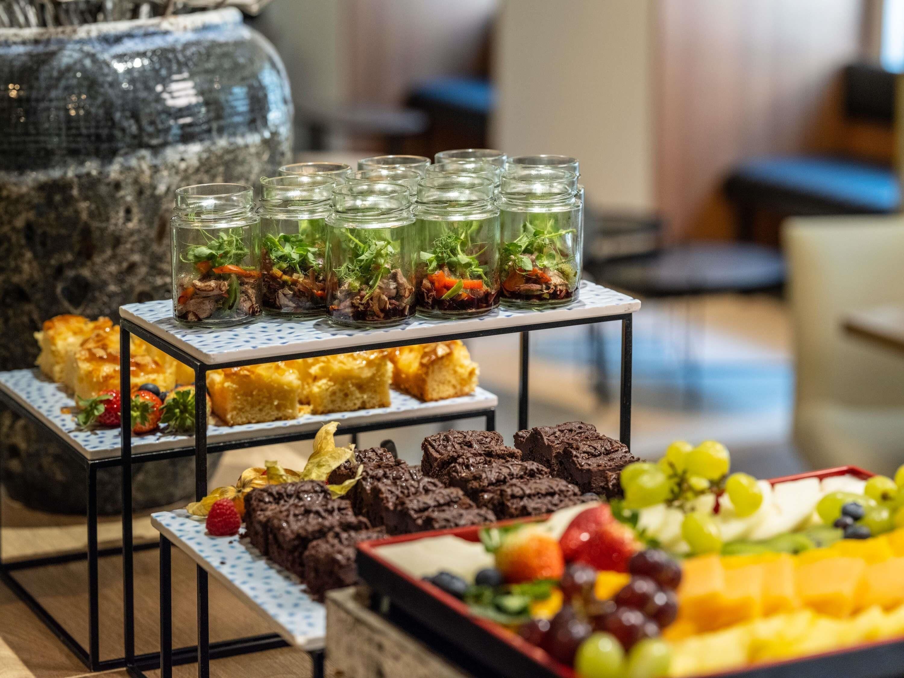 A buffet with various food items including desserts, fruits, and a glass terrarium with greenery.