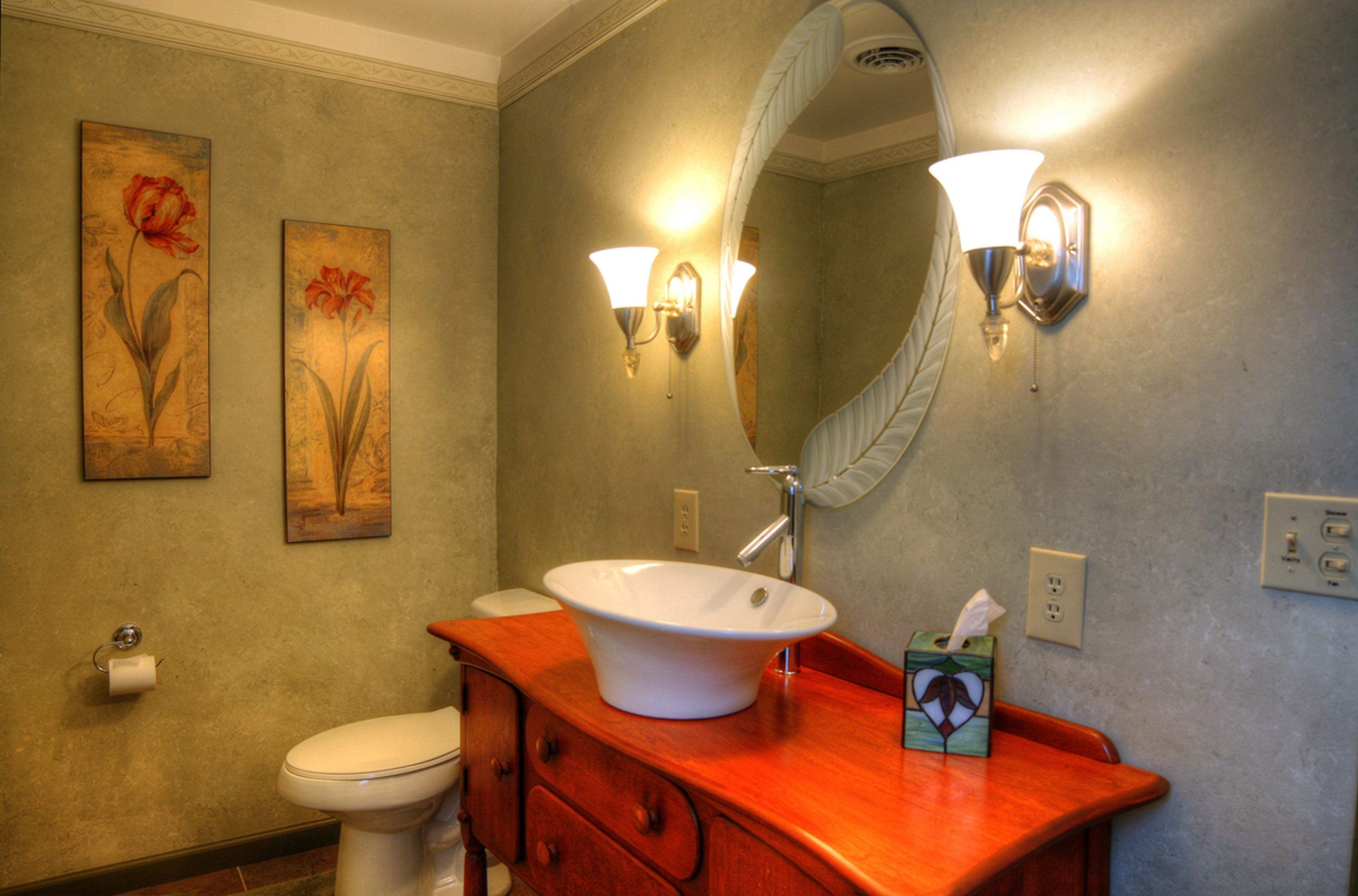 A bathroom with a white sink, wooden vanity, two wall-mounted light fixtures, and two floral paintings on the wall.