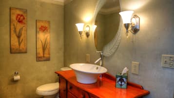 A bathroom with a white sink, wooden vanity, two wall-mounted light fixtures, and two floral paintings on the wall.