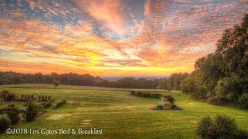 A rural landscape with a gazebo, open fields, and trees under a sunset sky.