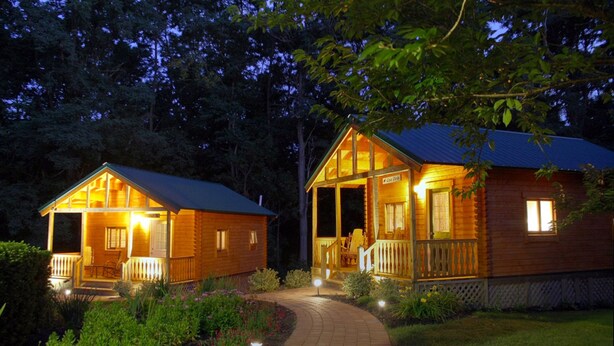 Dos cabañas de madera con porches, rodeadas de vegetación y un camino pavimentado que las conecta.