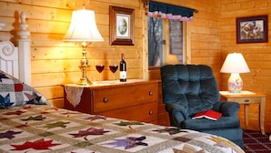 Acogedora habitación tipo cabaña de madera con cama, sillón, cómoda y ventana con vistas.