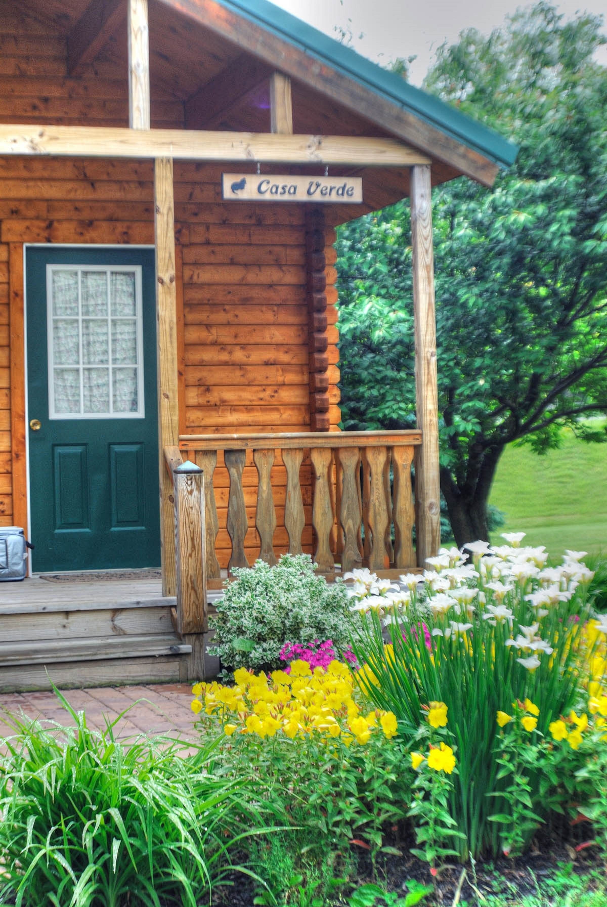 A wooden cabin with a green door, a porch with a railing, and a sign that reads "Casa Verde."