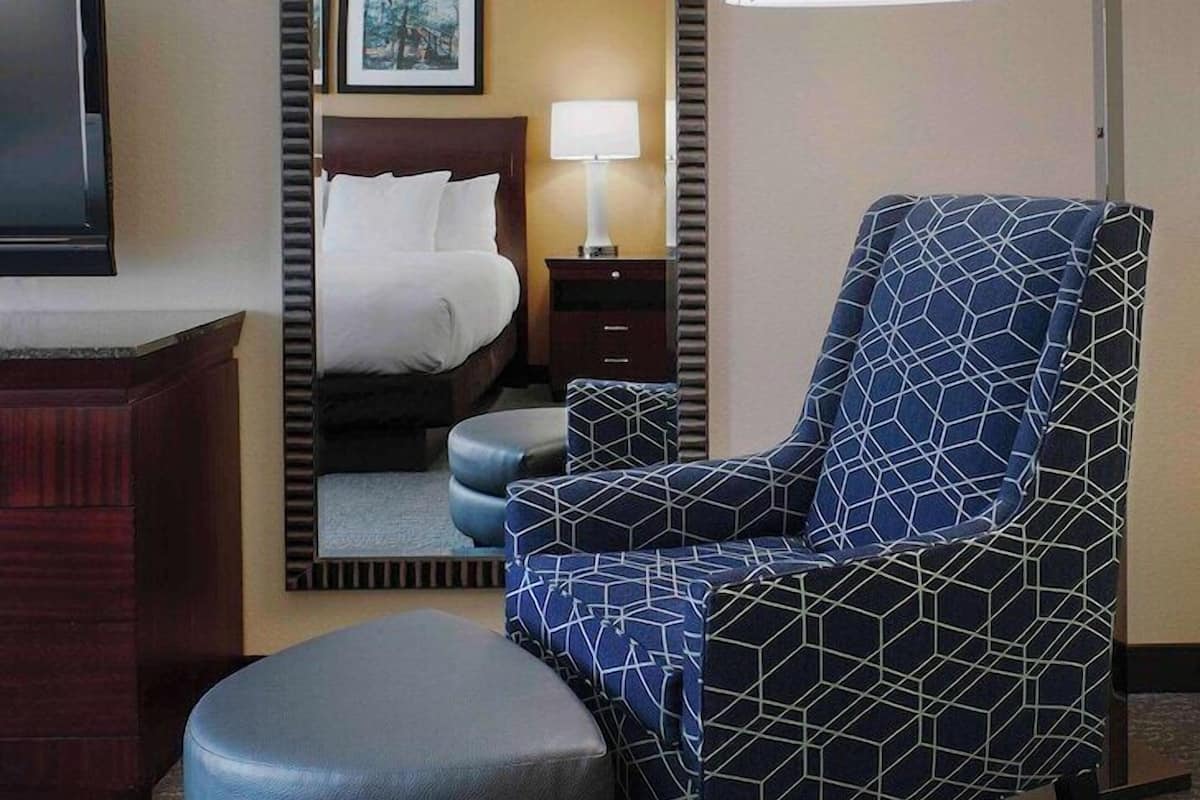 A hotel room with a bed, a chair, a lamp, and a television.
