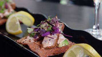 A dish with breaded fish topped with greens and sauce, accompanied by lemon slices.